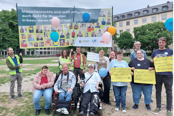 Eine Gruppe von Bewohnenden-Vertretungen und Unterstützungspersonen, die ein Banner mit Fotos hochhalten. Darauf steht: Menschenrechte sind nicht verhandelbar, auch nicht für Menschen in besonderen Wohnformen